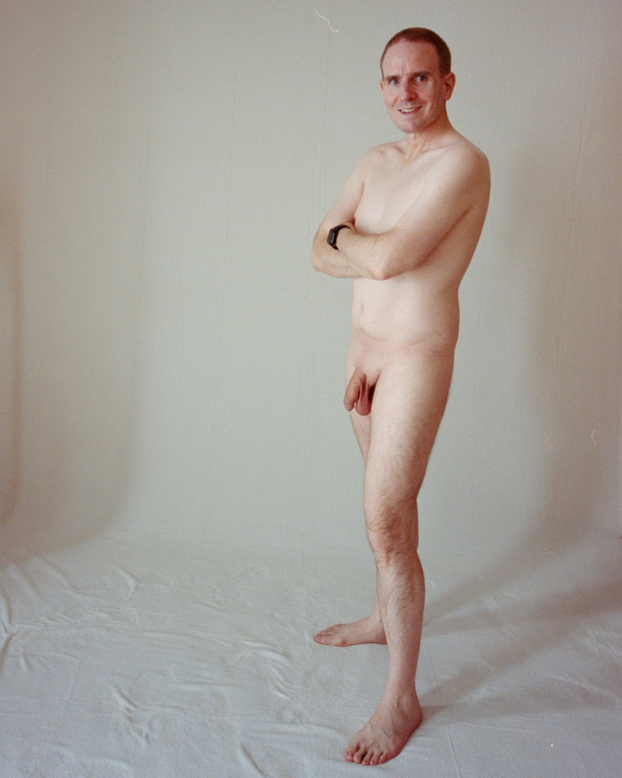 SJ Nude standing fully nude with arms crossed, white backdrop, San Jose