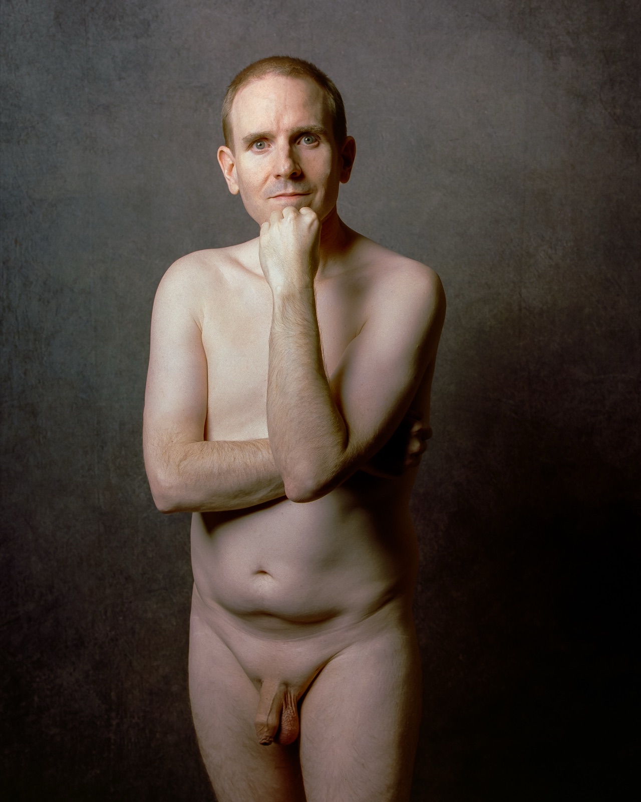 SJ Nude standing fully nude with a hand on his chin, gray backdrop, Portra 400, San Jose