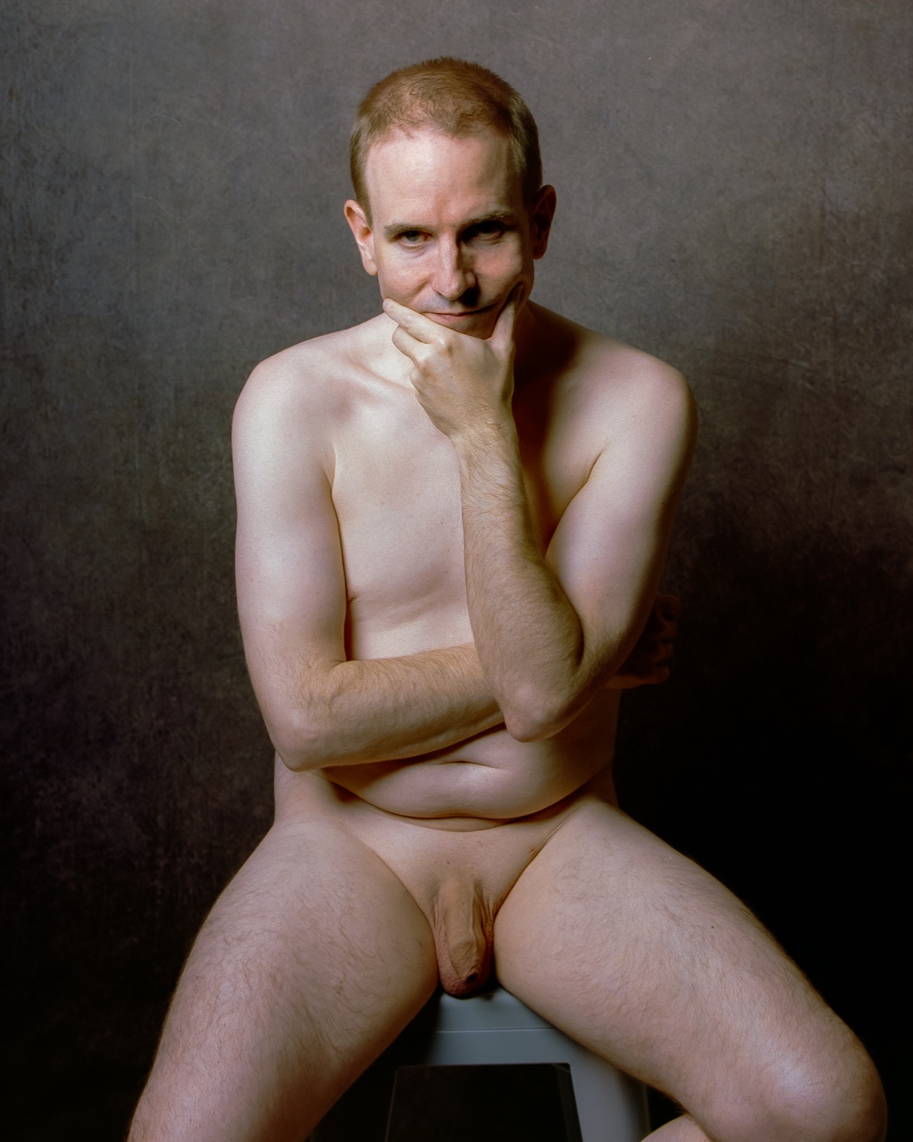 SJ Nude seated fully nude on a stool, hand on his chin, gray backdrop, Portra 400, San Jose